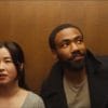 Glover and Esrkine standing next to each other in an elevator as they both look away from each other.